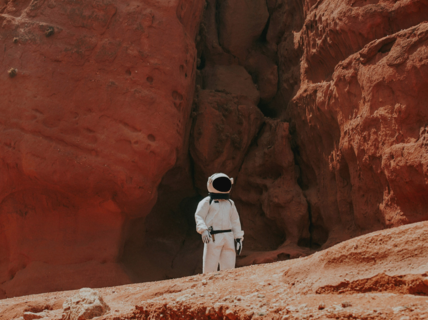 An astronaut in a space suit standing next to rock faces in a desert.