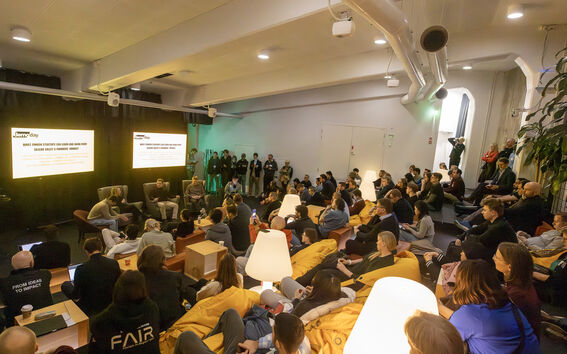 An image taking from the back of the room in Mordor auditorium. A panel discussion is taking place and a crowd is sitting and listening intently to it.