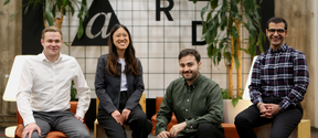 The Deltan Labs team at the A Grid premises. 4 people (3 men and 1 woman) sitting down smiling at the camera