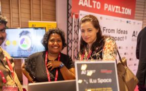 Two women in the center, on of them looking at the camera and similing, the other one checking the laptop looking down at it. Picture taken at Dipoli, the event place where NORDEEP happens
