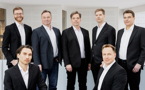 The PulseOn team posing for the camera. 7 men in suits, 5 standing and 2 sitting on the sides